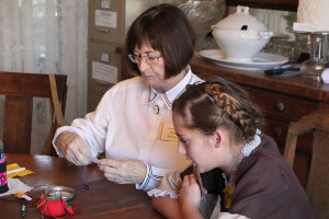 Farmersville Historical Society member Pansy Anderson aids 5th grade student Tatum De Hart in sewing a special 2015 ornament at the Farmersville 1900s program.
